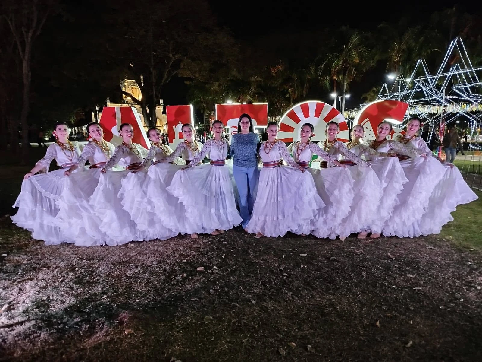 Grupo de Margaret Weberhofer Estudio de Danza con vestuario blanco de danza paraguaya al aire libre por la noche